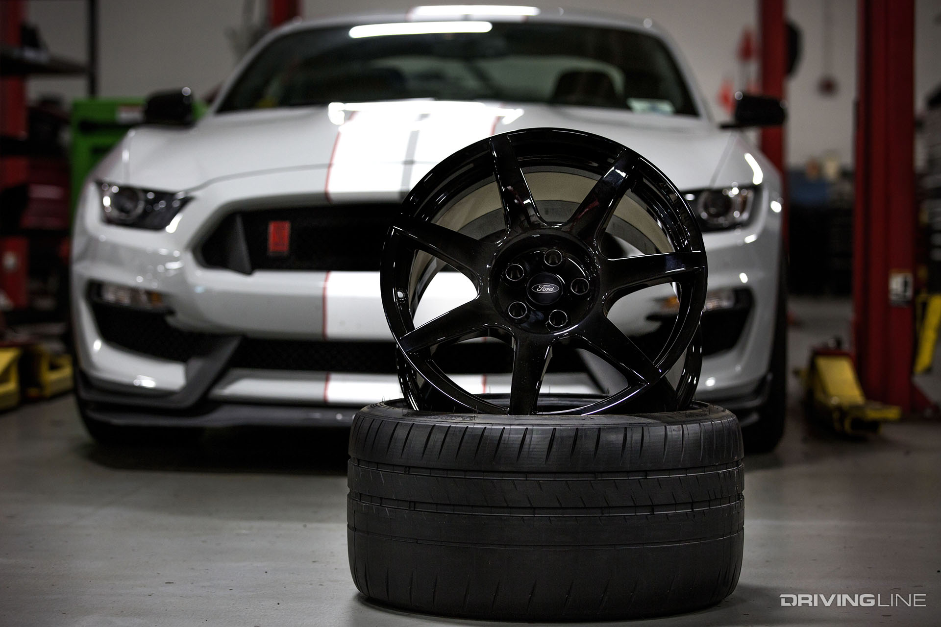 Two wheels and tires in front of a grey Ford Mustang with white racing stripes