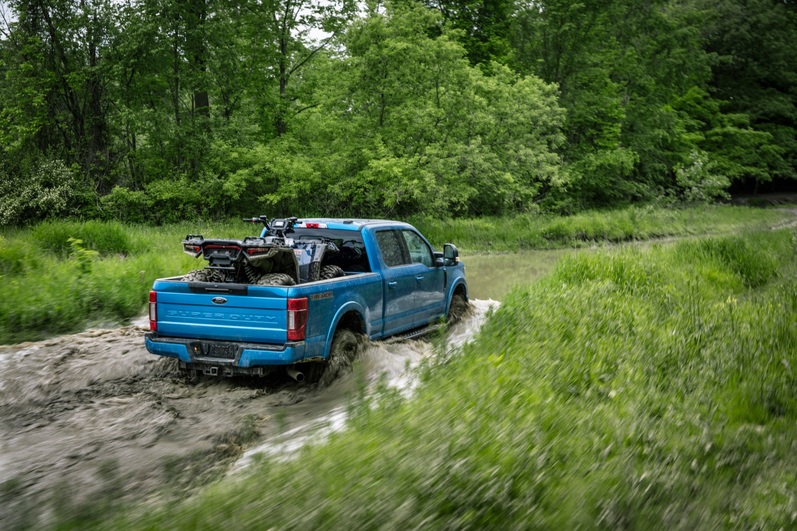 Ford F250 with an ATV in the bed driving through a swamp