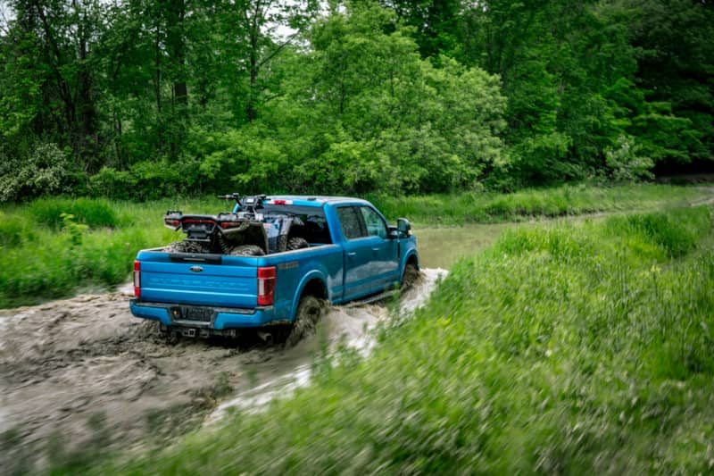 Ford F250 with an ATV in the bed driving through a swamp