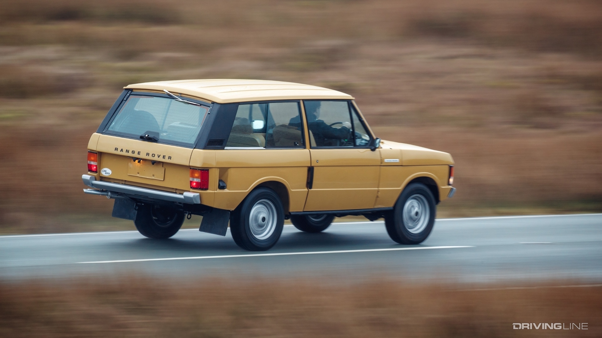 Yellow Land Rover Range Rover Classic driving down highway.