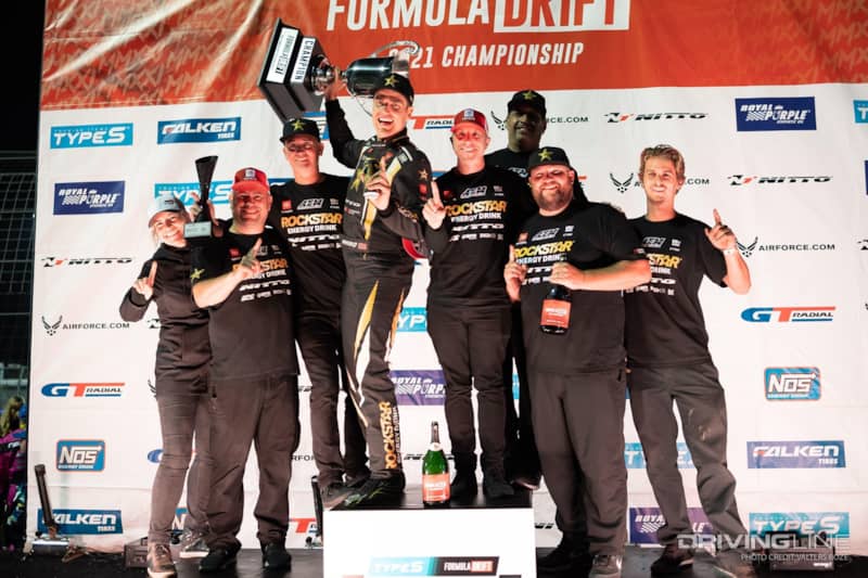 Fredric Aasbo holding up the championship trophy on the podium surrounded by his team