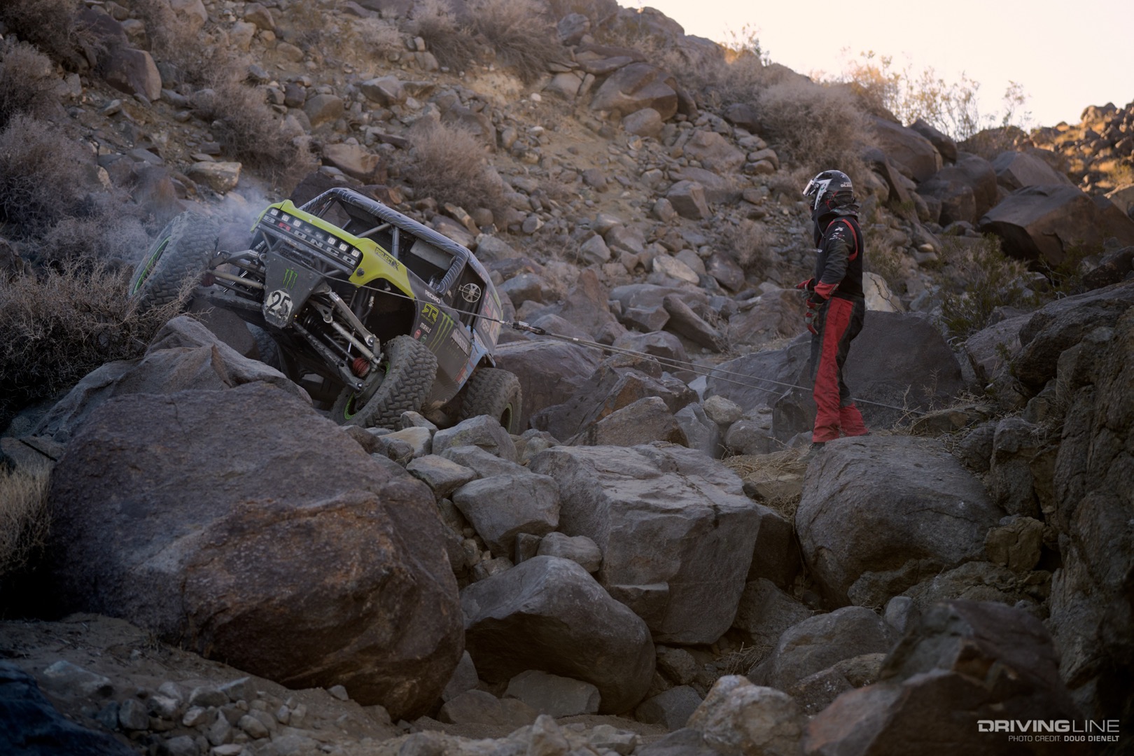 Vaughn Gittin Jr. winching with his co-driver out of the car by the rock that his winch line is tied to