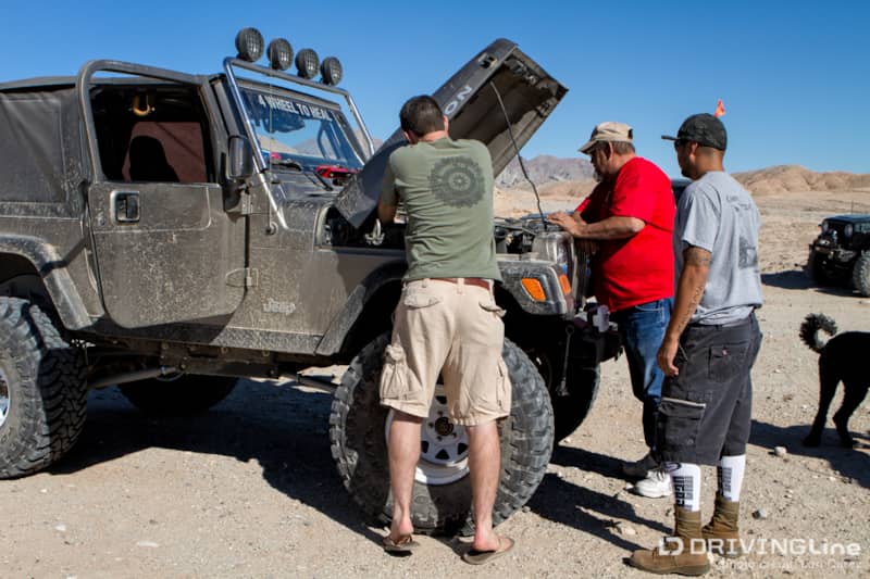 Three men fixing a Jeep Wrangler with the hood up