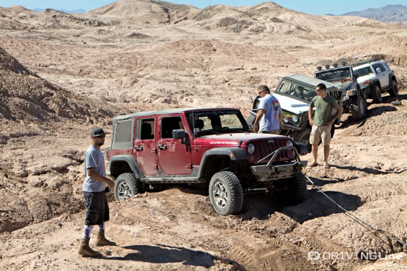 A four-door Jeep Wrangler being towed out of being high-centered with a line of rigs behind it