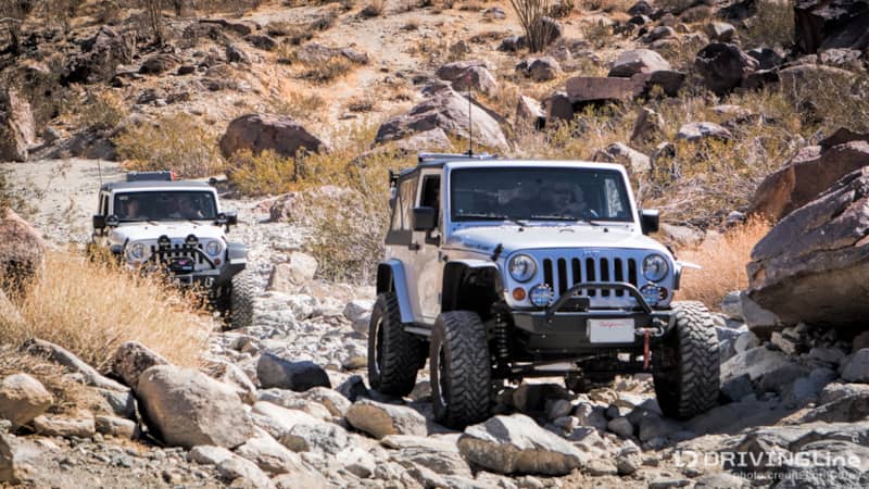 Two Jeep Wranglers driving over rocks on a trail