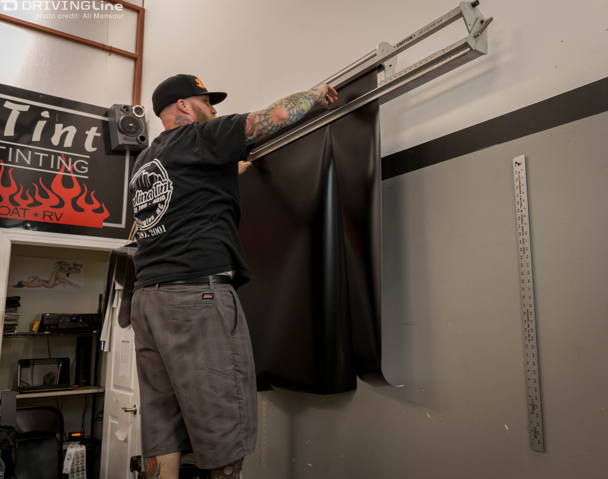 Man haging up 3M 1080 Satin Black vehicle wrap on a wrack