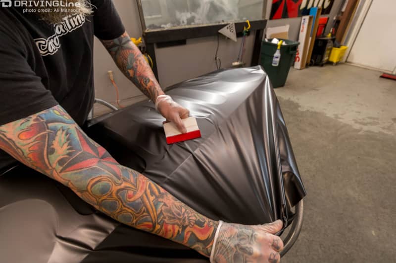 Man using a squeegee to install the 3M 1080 Satin Black vehicle wrap on the Jeep Wrangler JK door