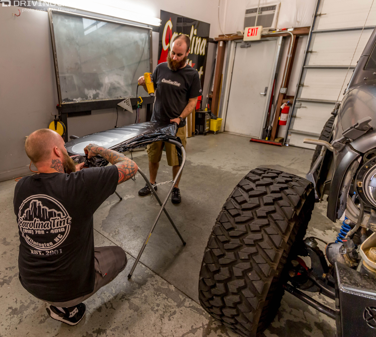 Two men installing a 3M 1080 Satin Black vehicle wrap on a small part of a Jeep Wrangler JK