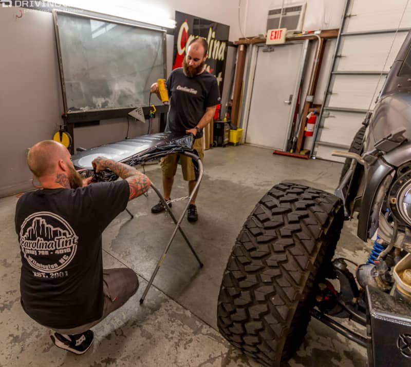 Two men installing a 3M 1080 Satin Black vehicle wrap on a small part of a Jeep Wrangler JK