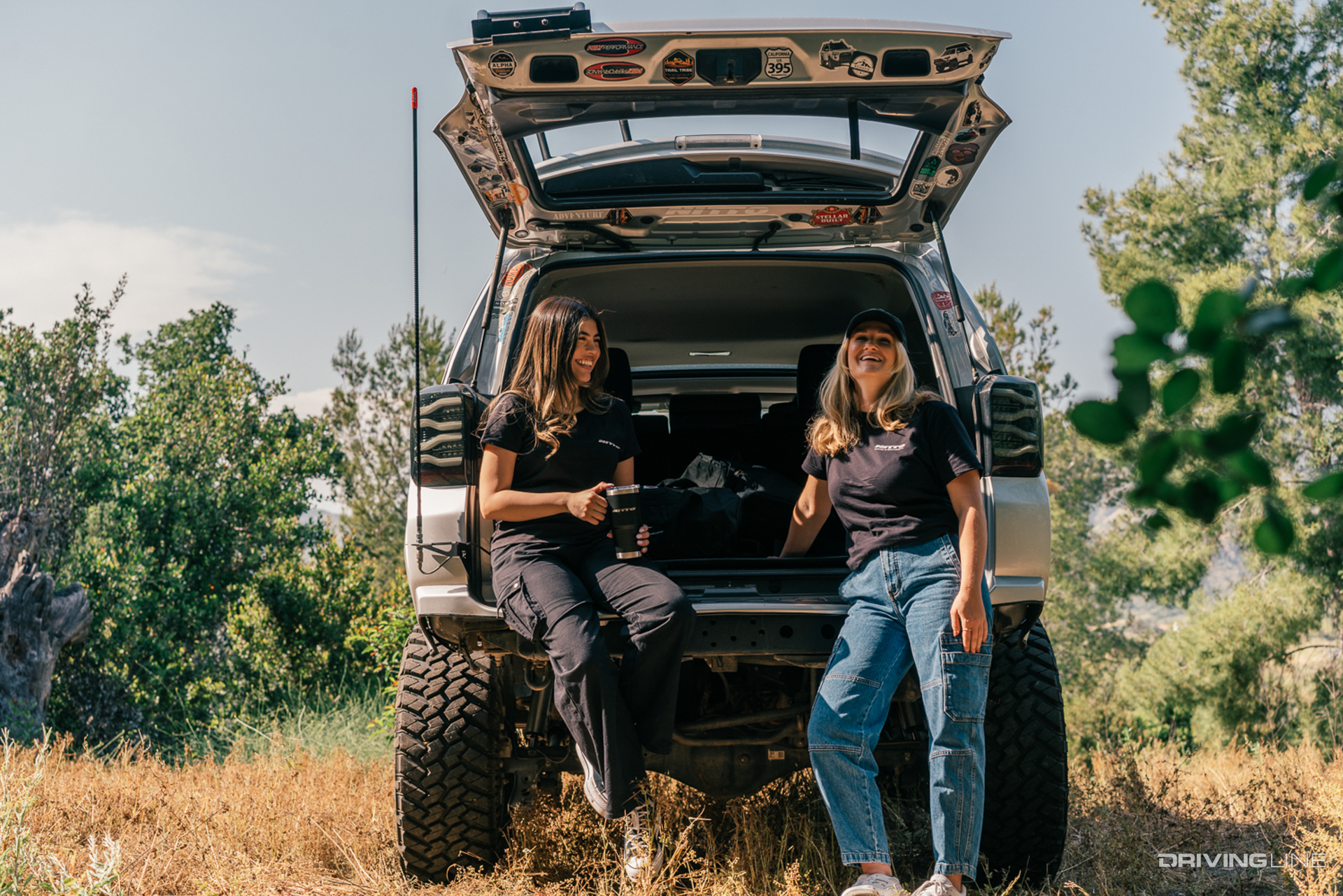 Two people in Nitto branded clothing in forest in front of off-road vehicle